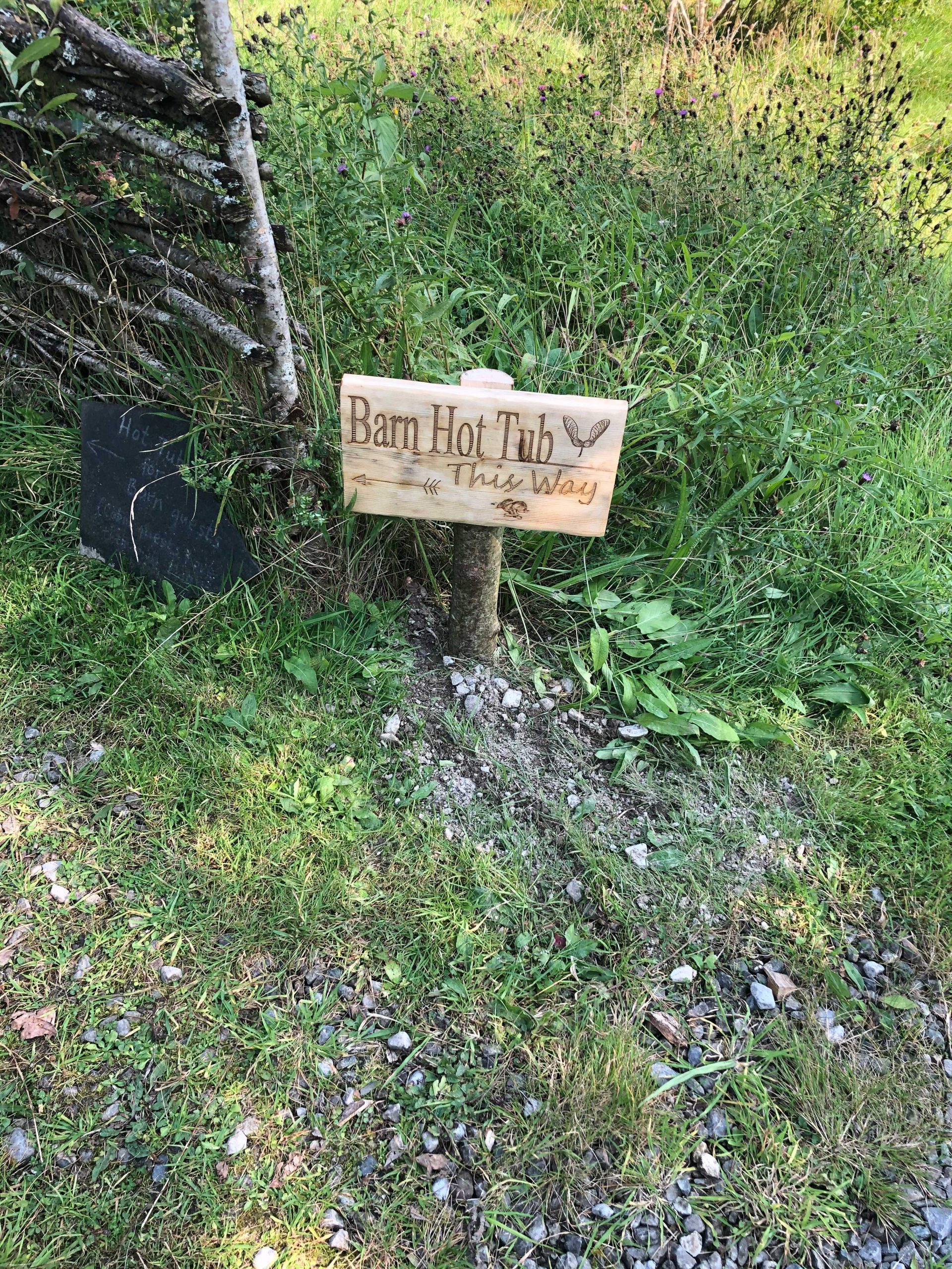 Rustic wooden sign in woods reads Barn Hot Tub This Way